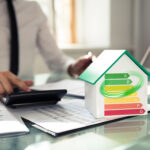 Mortgage lender sitting at desk using a calculator, with a house and EPC graph on a desk with papers
