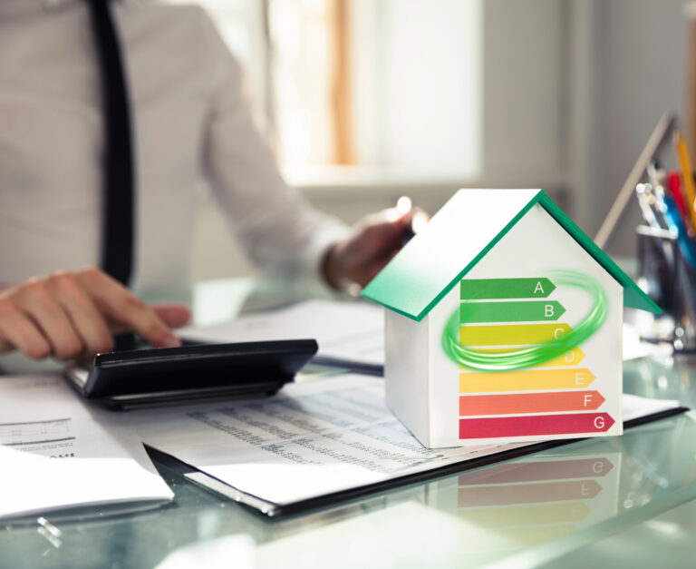 Mortgage lender sitting at desk using a calculator, with a house and EPC graph on a desk with papers