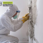 biological suited person with a mask repairing mould inside on a wall with a nottingham sity council logo