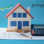 A model house next to a calculator and pen sitting on a spreadsheet, paragon logo