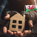 Homeless man holding a cardboard cutout of a house and a welsh flag