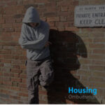 Muted photo with a youth in a hoodie leaning up against a wall