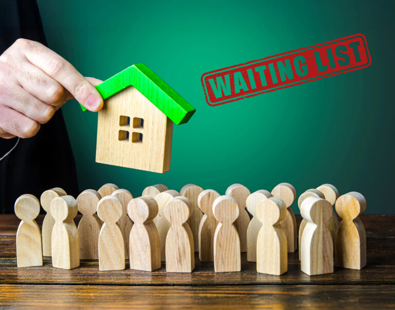 wooden House being held above wooden people with a waiting list stamp