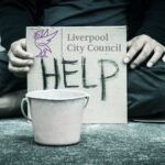 Cardboard sign reading “HELP” with Liverpool City Council logo, symbolising homelessness support efforts.