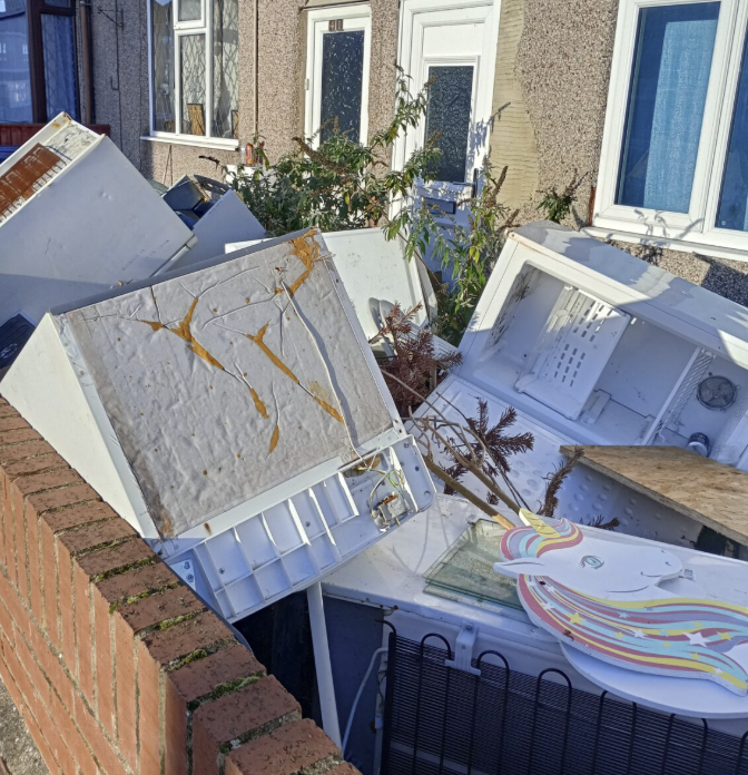Pile of discarded fridges and waste dumped in front garden of empty house