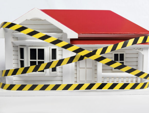 Model house wrapped in caution tape symbolizing unsafe housing enforcement.