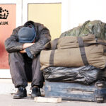 Person sitting on street beside bags, illustrating homelessness in the UK.