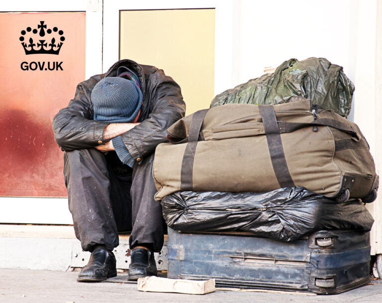 Person sitting on street beside bags, illustrating homelessness in the UK.
