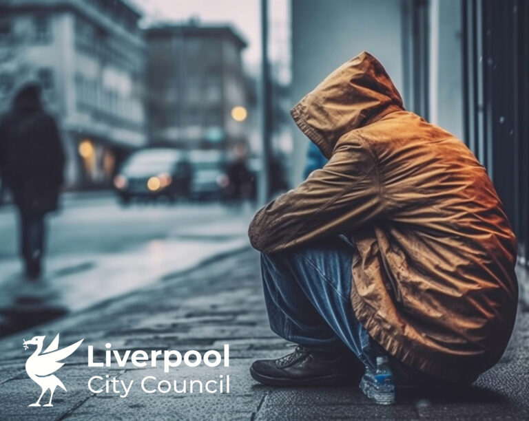 Person in a hooded jacket sitting on a city street, highlighting homelessness in Liverpool.