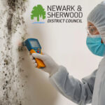 Council worker inspects mould on wall with moisture meter as part of damp investigation.