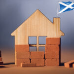 Wooden house model with Scottish flag symbolising Scotland’s housing crisis and construction challenges