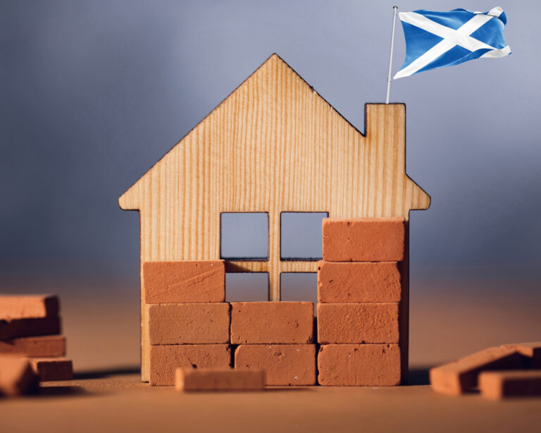 Wooden house model with Scottish flag symbolising Scotland’s housing crisis and construction challenges