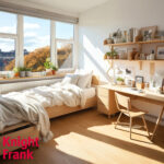 Modern student bedroom with desk, shelving, and large window overlooking city rooftops.