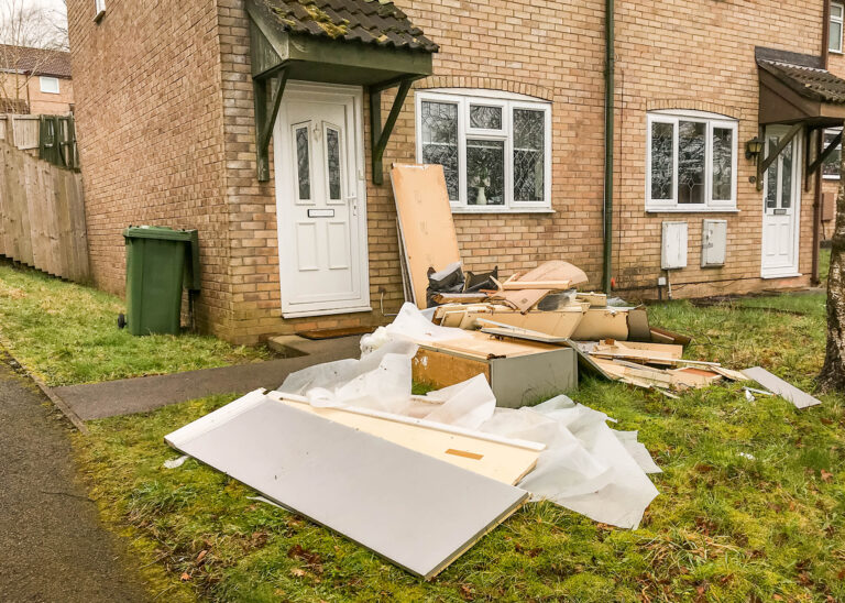 Debris and damaged furniture outside a brick house after property fire and cleanup.