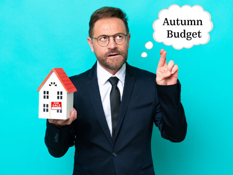 Estate agent holding house model with ‘Autumn Budget’ thought bubble, symbolising property tax uncertainty