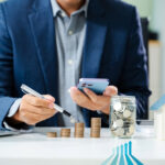 Businessman reviewing housing investment with stacked coins and savings jar.