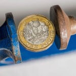 Pound coin squeezed in a clamp symbolising financial pressure on landlords