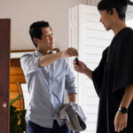 Father handing house keys to son in graduation gown, symbolizing parental property investment for students