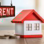 Model house with coins and rent sign symbolizing property rental yields and refinancing challenges