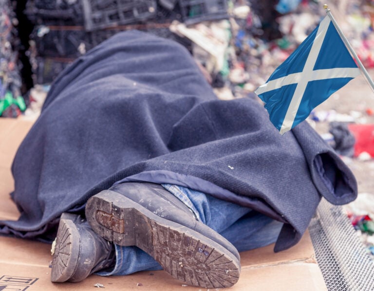 Person sleeping rough under a blanket with Scottish flag symbolizing housing crisis