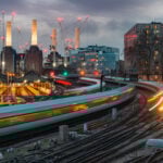 Trains passing Battersea Power Station at dusk with city lights and cranes in the background