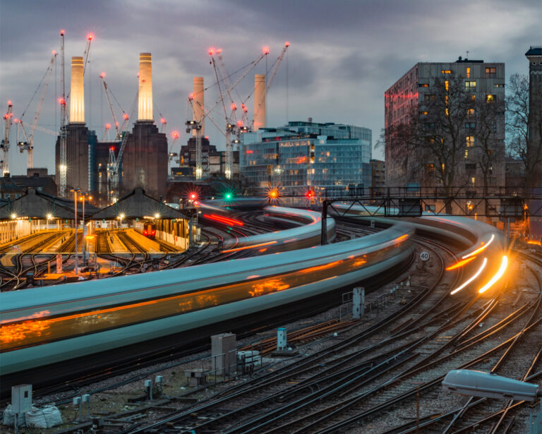 Trains passing Battersea Power Station at dusk with city lights and cranes in the background