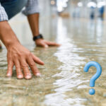 Man inspecting water damage on floor with question mark symbolizing uncertainty about repairs.