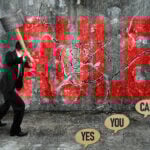 Businessman smashing the word "RULE" on a wall with a sledgehammer, symbolizing breaking unfair rules.