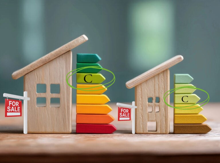 Two wooden house models beside colorful energy rating charts showing EPC grade C and “For Sale” signs.