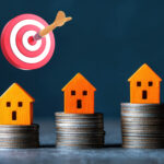 Three small house models on coin stacks with a target and dart symbolizing London housing goals.