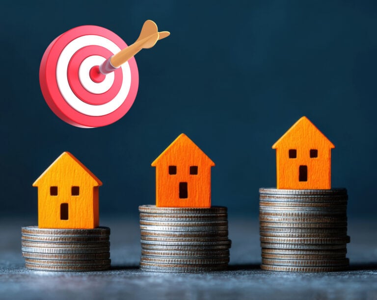 Three small house models on coin stacks with a target and dart symbolizing London housing goals.