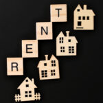 Wooden houses and letter tiles spelling “RENT” on a black background, symbolising the UK rental housing market.