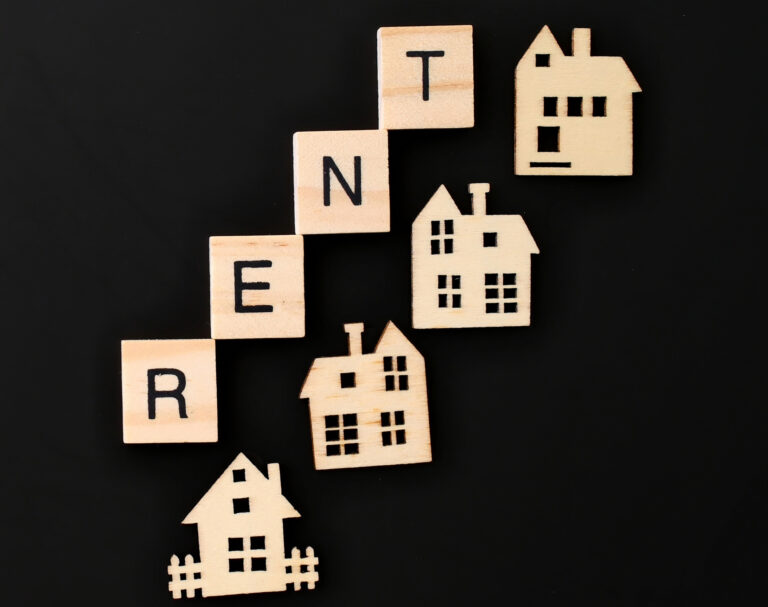 Wooden houses and letter tiles spelling “RENT” on a black background, symbolising the UK rental housing market.