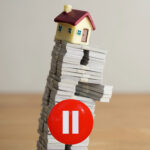Model house on a leaning stack of documents with a red pause button symbolising a slowdown in buy-to-let lending.