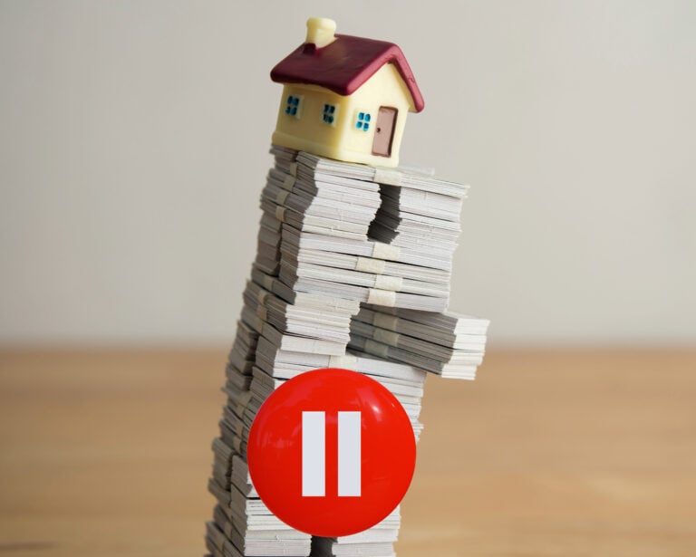 Model house on a leaning stack of documents with a red pause button symbolising a slowdown in buy-to-let lending.