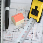 Model house, ruler, and tape measure on architectural blueprints symbolizing housing and planning reforms