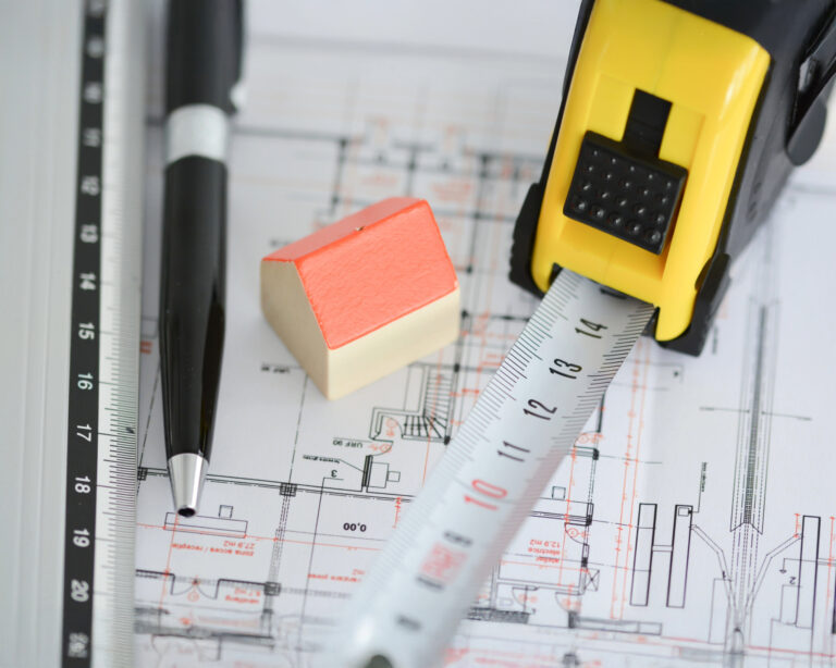 Model house, ruler, and tape measure on architectural blueprints symbolizing housing and planning reforms