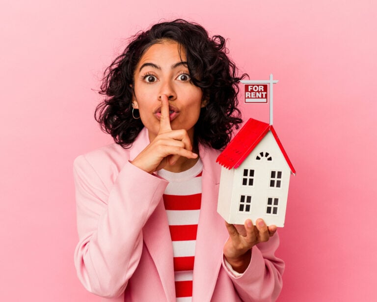 Woman signaling for silence while holding a model house with a "For Rent" sign.