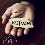 Hand holding torn paper with the word “asylum,” symbolising housing for asylum seekers amid rental market changes