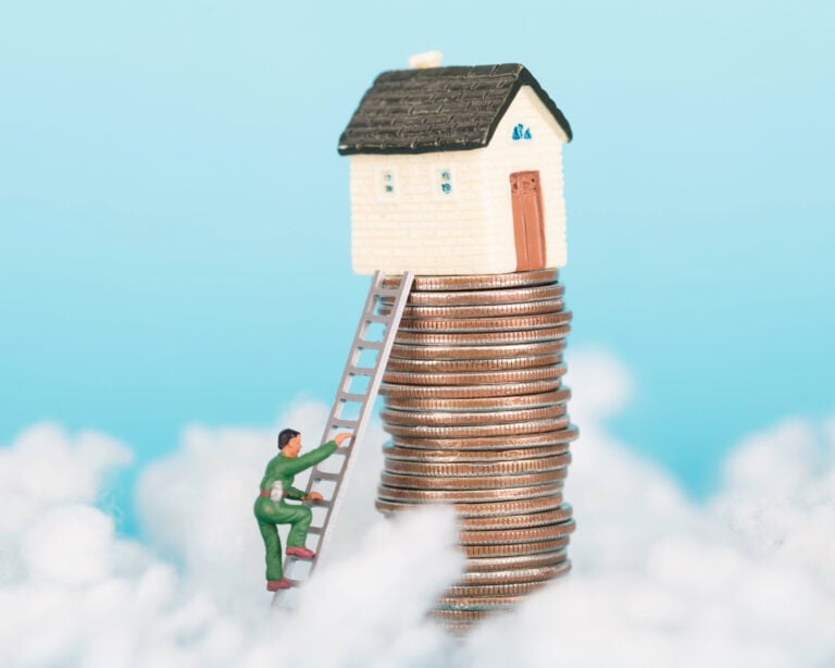 Miniature man climbs ladder toward house atop stacked coins symbolizing rising UK property prices.