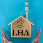 Wooden house model with LHA letters symbolising Local Housing Allowance and rent support reform.