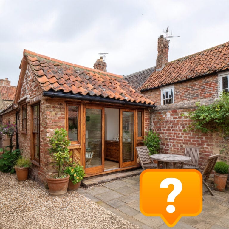 Small brick annexe with patio and wooden doors in a cottage garden setting