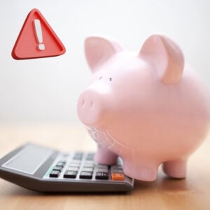 Piggy bank on a calculator beside a warning symbol highlighting risks in tenancy deposit calculations