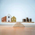 Wooden houses and stacked coins balanced on a seesaw representing UK housing market uncertainty