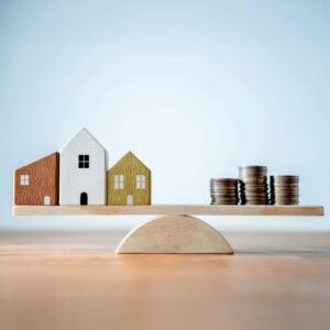 Wooden houses and stacked coins balanced on a seesaw representing UK housing market uncertainty