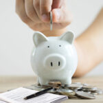 Hand placing a coin into a piggy bank to illustrate saving toward a rental deposit