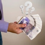 Hand holding a large bundle of banknotes with question marks above, illustrating uncertainty about rent and UC payments