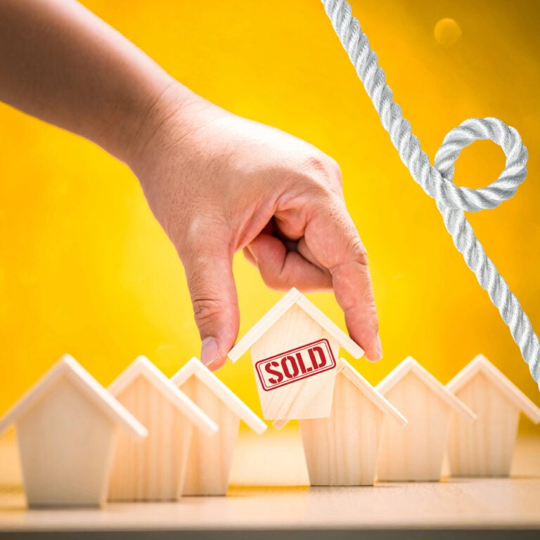 Hand selecting a wooden house marked “Sold” to illustrate council buyback costs