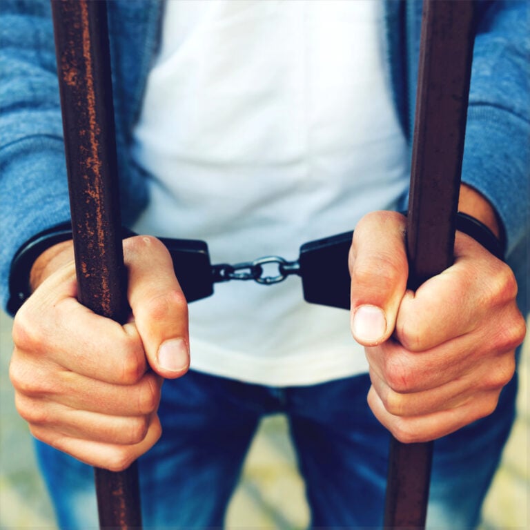 Hands in handcuffs gripping prison bars, symbolising legal trouble for landlords without proper licences