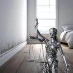 Blindfolded Lady Justice statue standing in a damp, mould-affected rental property